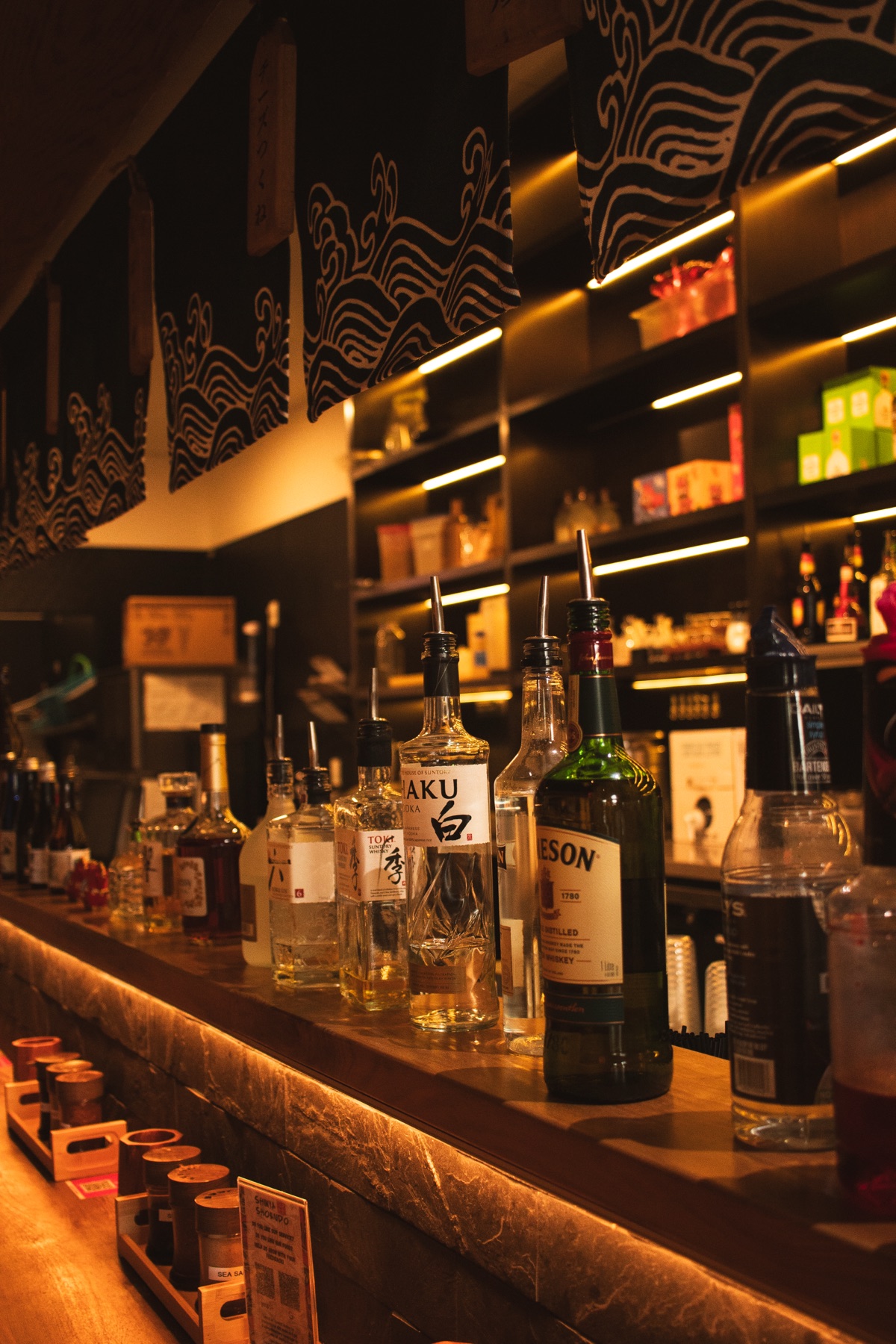 Back bar shelf of Japanese whisky and sake beneath a wave mural