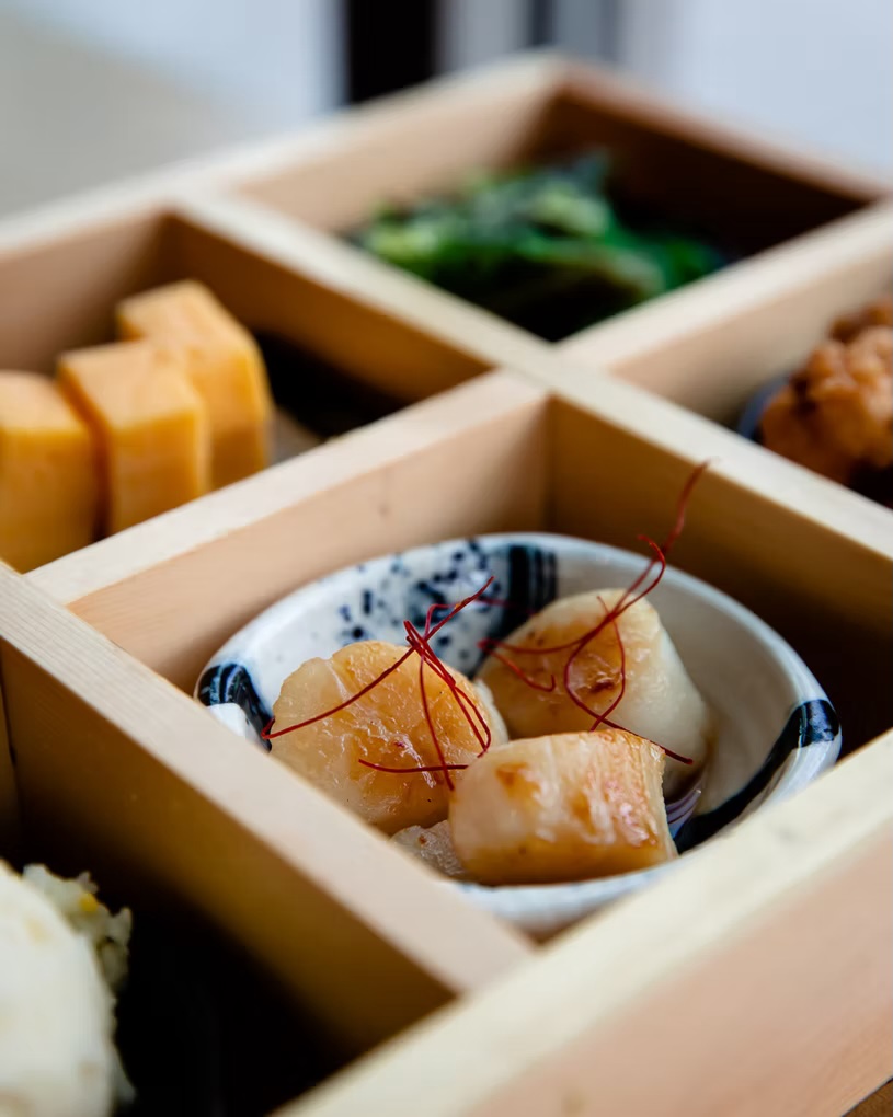 Bento compartments with scallops, tamagoyaki and greens in a wooden box