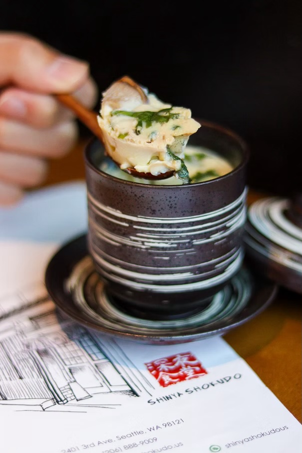 Spoonful of steamed egg custard lifted from a striped ceramic cup