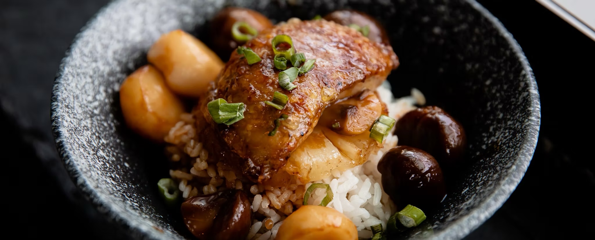 Glazed chicken over rice with chestnuts in a black stone bowl