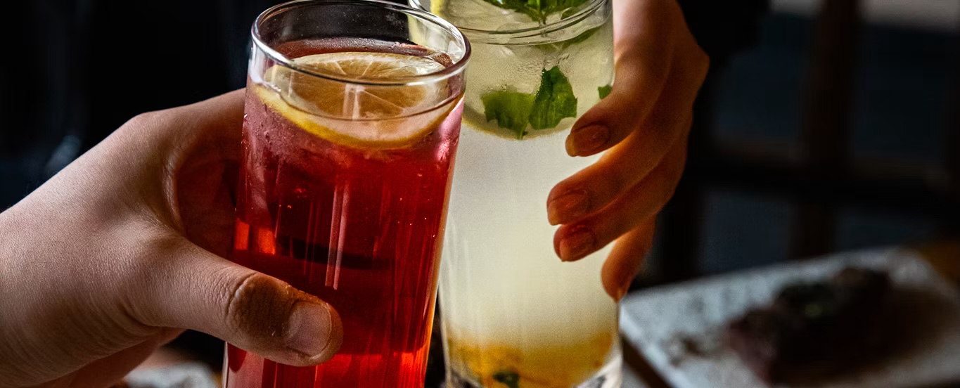 Two hands toasting with fruit tea and a mint cocktail