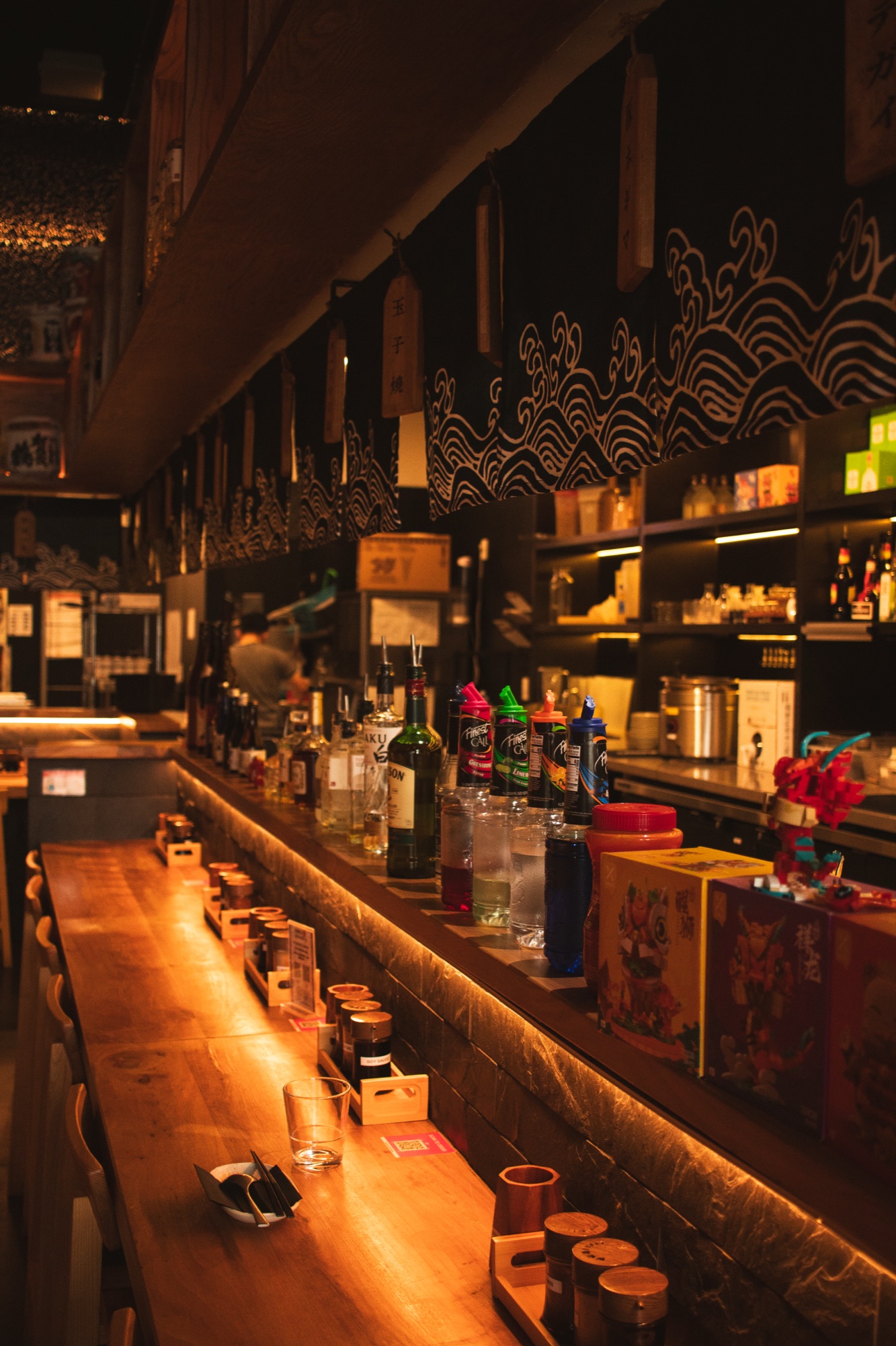 Warmly lit bar counter stretching down the izakaya at night
