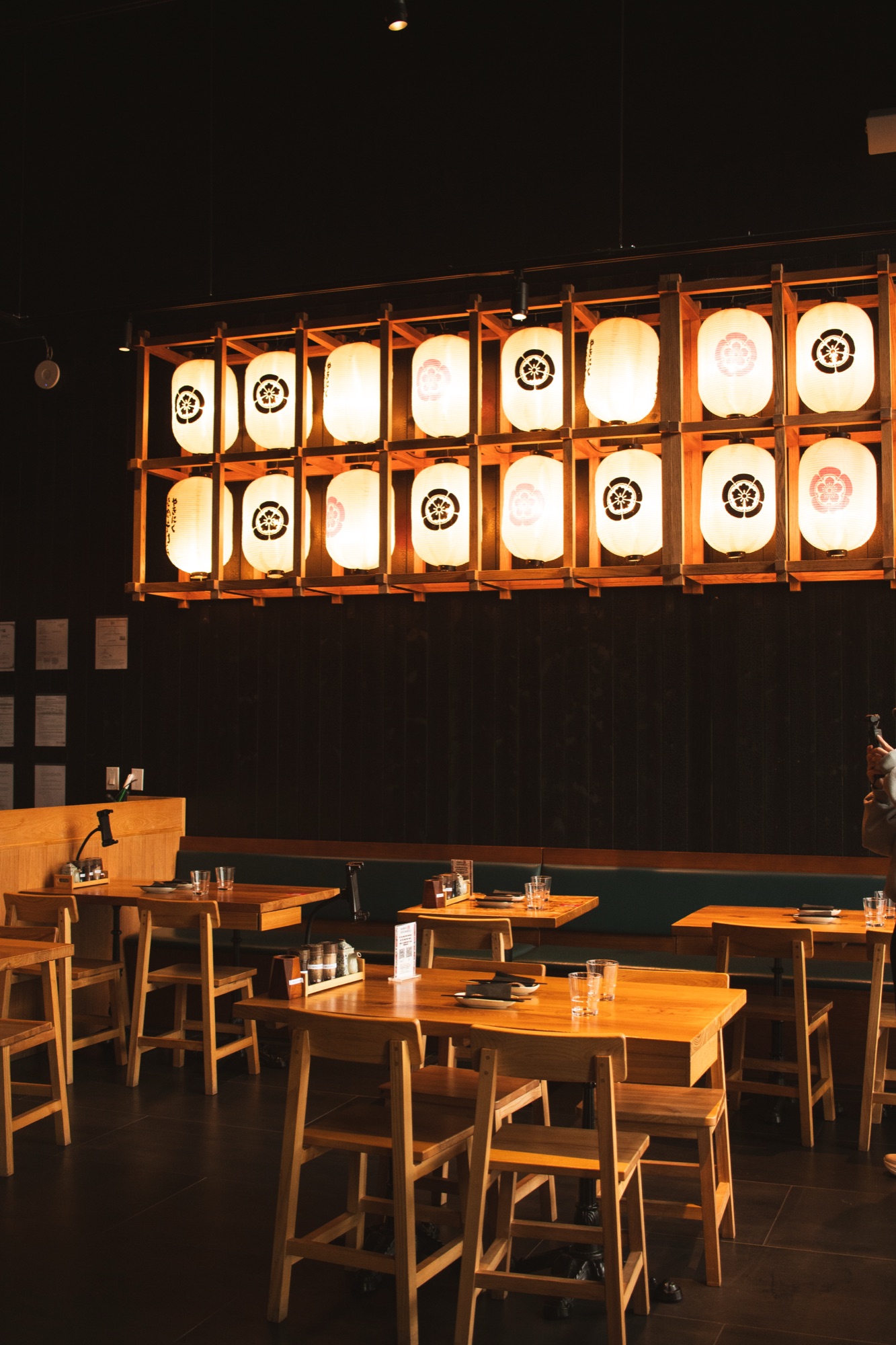 Dining room with warm wooden tables beneath a wall of glowing white lanterns