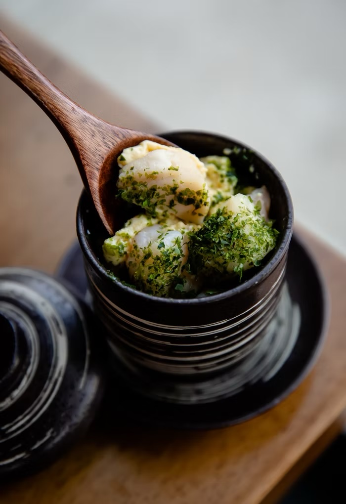 Scallops dusted with green herbs in a striped ceramic cup