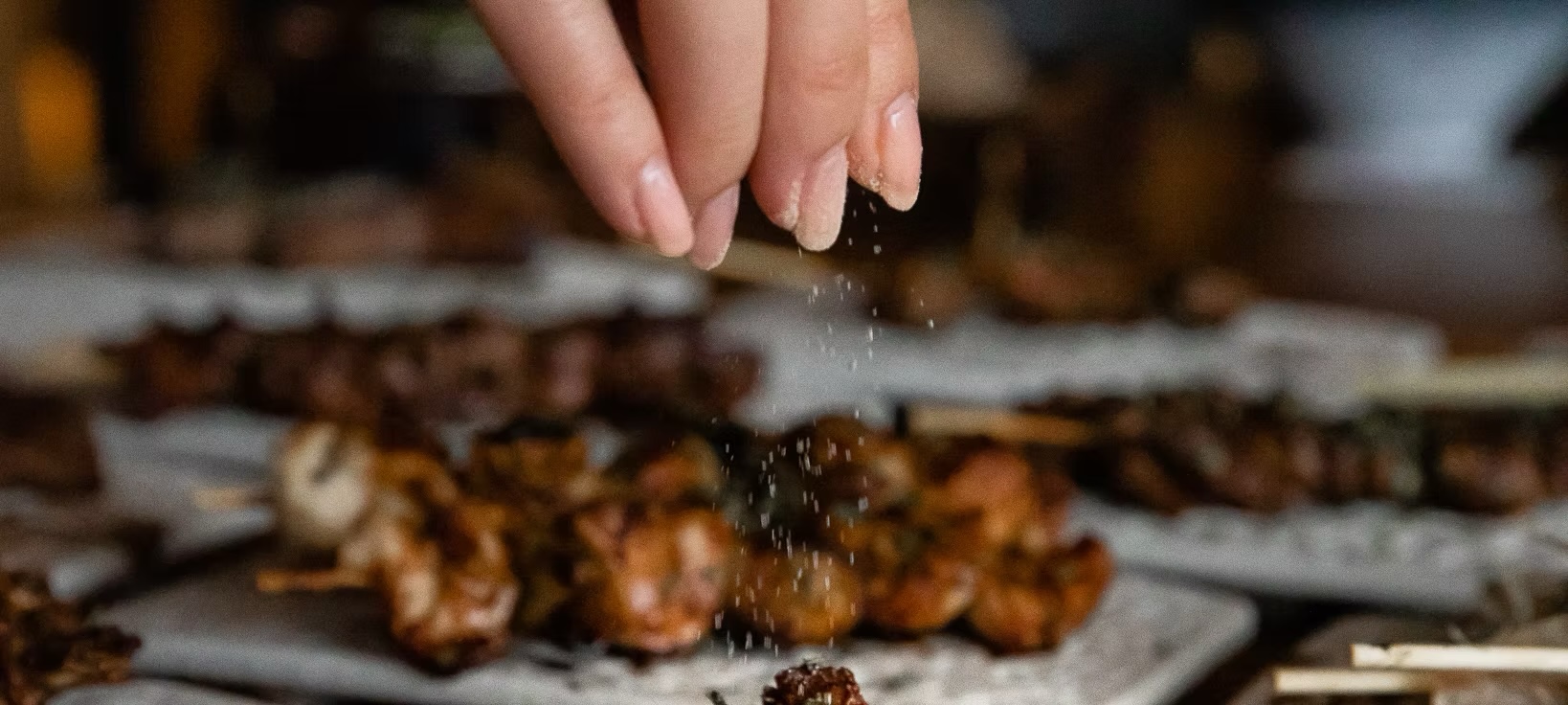 Hand seasoning rows of grilled skewers during evening service