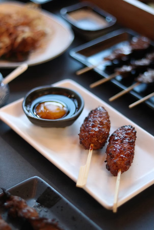 Glazed skewers beside a dish of egg yolk soy sauce